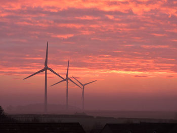 Silhouette of wind turbines against dramatic sky during sunset