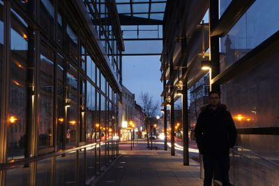 Man standing on sidewalk in illuminated city at dusk