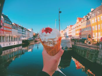 Cropped hand holding ice cream over canal in city