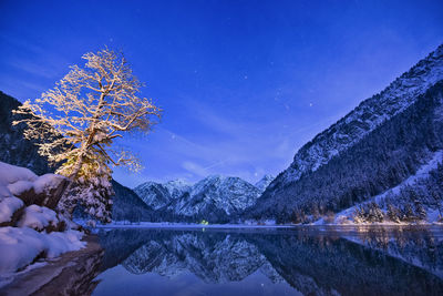 Scenic view of lake by snowcapped mountains against blue sky