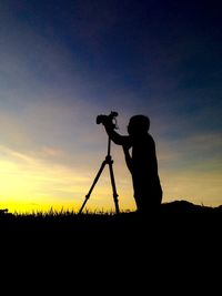 Silhouette person photographing on field against sky during sunset