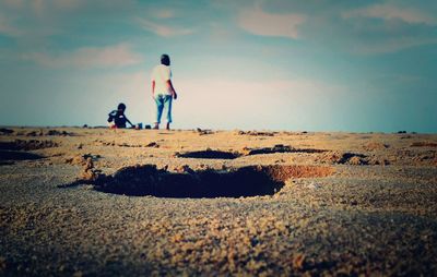 Side view of two people on land against sky