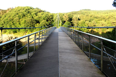 Footbridge along plants and trees against sky