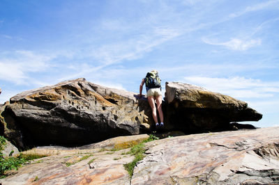 Low section of female hiker with backpack standing on rock formation against sky during sunny day