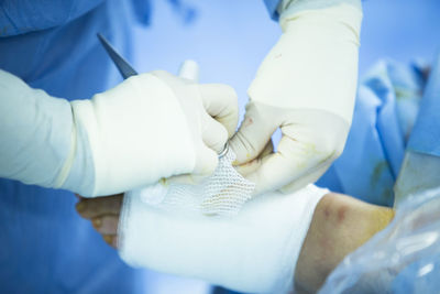 Midsection of doctor applying adhesive bandage on patient leg in hospital