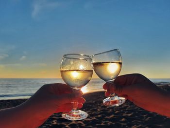 Close-up of hand holding wineglass against sea against sky