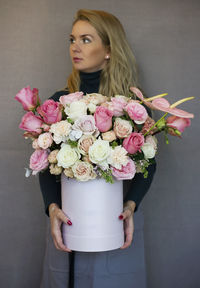 Woman holding flower bouquet while standing against gray wall