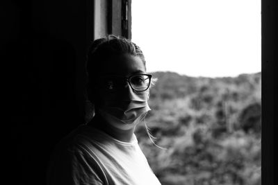 Portrait of young woman wearing mask against window 