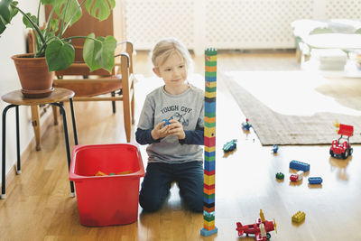 Smiling girl looking at toy blocks while kneeling on floor at home