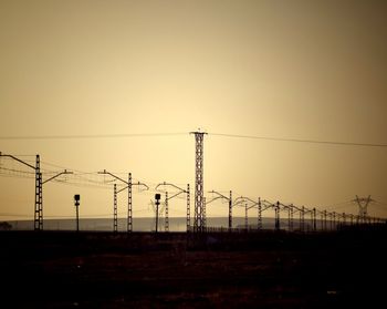Silhouette electricity pylons on landscape against clear sky