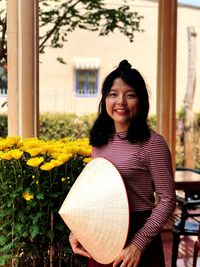 Portrait of woman smiling while holding asian style conical hat outdoors