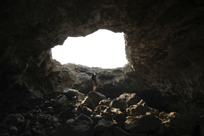 Low angle view of man standing on rock in cave against clear sky