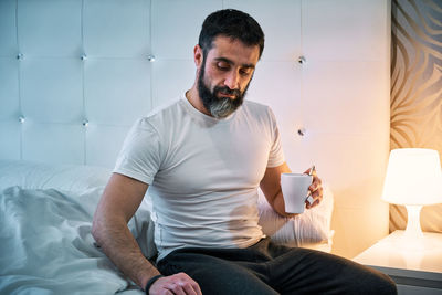 Person with some kind of problem sitting on the bed with a cup and looking at the floor