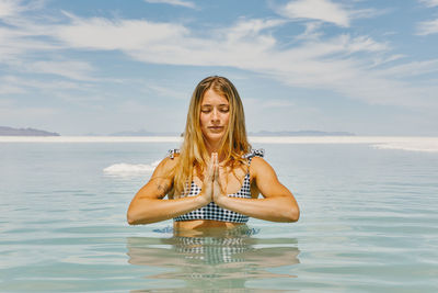 Young woman meditating in water in bonneville salt flats.