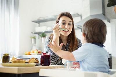 Mother feeding breakfast to son at table in kitchen