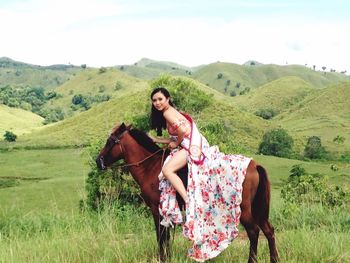 Portrait of smiling young woman with horse on field against sky