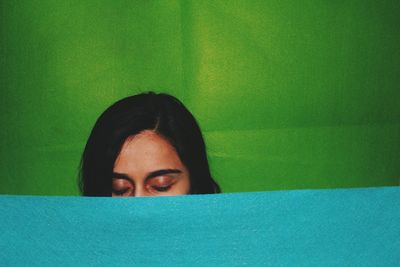 Close-up of woman with eyes closed amidst green and turquoise fabrics