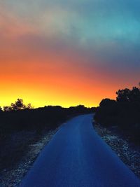 Road amidst silhouette trees against orange sky