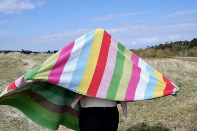  person with multicolored flag on field against sky