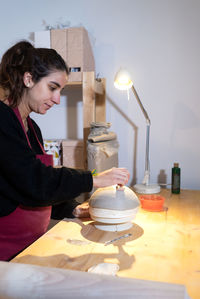 Young ceramist woman marking ceramic bowl in pottery workshop