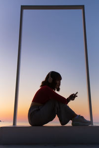 Side view of woman using smart phone against sky