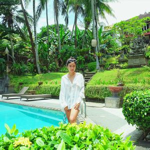 Portrait of young woman standing by swimming pool against trees