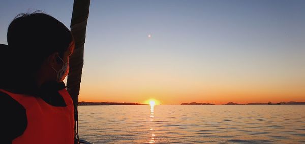 Rear view of woman against sea during sunset