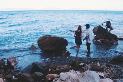 People standing on rocks by sea against clear sky