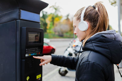 Side view of young woman listening to music using parking meter