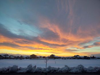 Snow covered landscape against sky during sunset