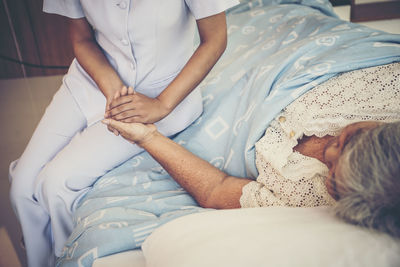 Midsection of nurse holding hand of female senior patient relaxing on bed in hospital