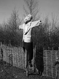 Scarecrow by fence on field against bare trees