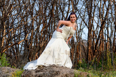 Full length of young woman standing in forest in wedding dress