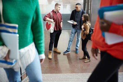 Friends talking while standing in corridor with female university students in foreground