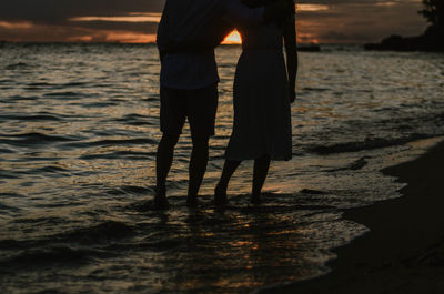 Low section of silhouette people standing at beach