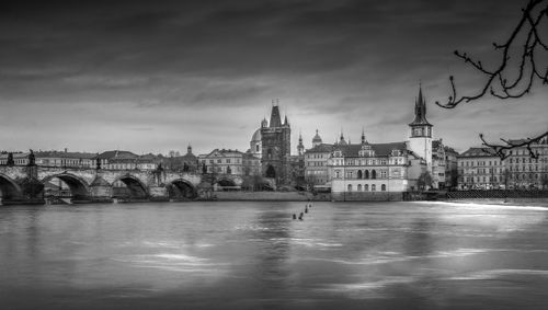 View of buildings by river against cloudy sky