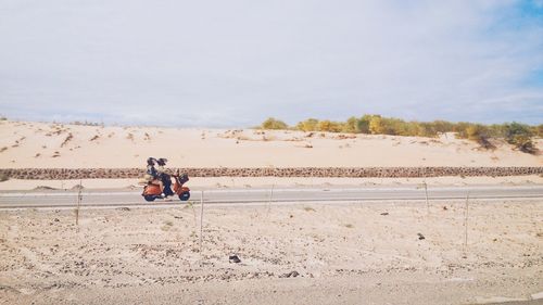 Man and woman riding on scooter in barren landscape