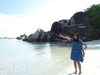 Full length of young woman standing at beach against sky during sunny day