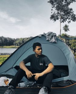 Young man sitting on car against sky