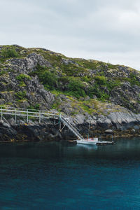 Motorboat moored near rock formation by sea against sky
