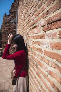 Side view of happy woman standing by brick wall