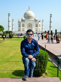 Portrait of man wearing sunglasses sitting against taj mahal