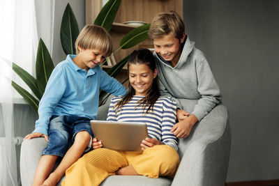 The beautiful dark-haired sister and her brothers are sitting at home on the couch, playing games 