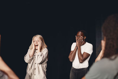 Multiracial male and female stage performers with heads in hands practicing emotions together in class