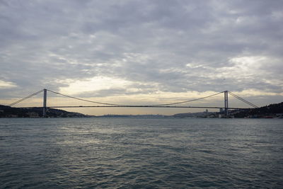 Low angle view of bosphorus bridge over sea against cloudy sky