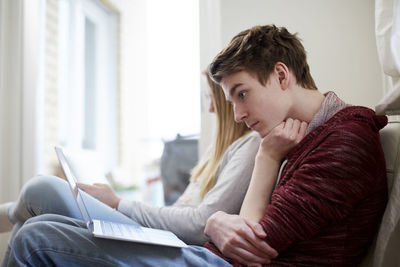 Teenage boy watching laptop while sitting by sister in living room at home