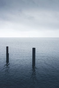 Wooden posts in sea against sky