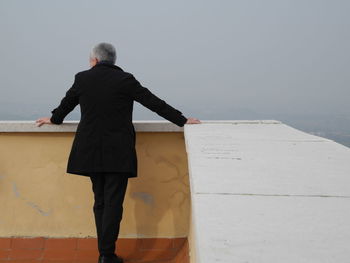 Rear view of mature man standing on building terrace against clear sky