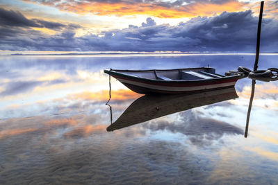 Boat moored in lake against sky during sunset