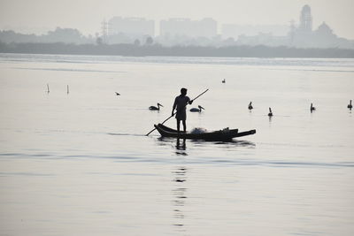 Silhouette man rowing boat in sea against sky